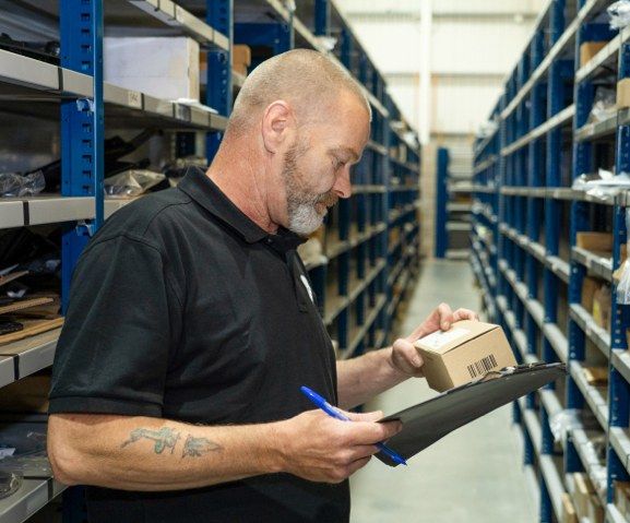 A TPS warehouse colleague checking a parts order in the stock aisles